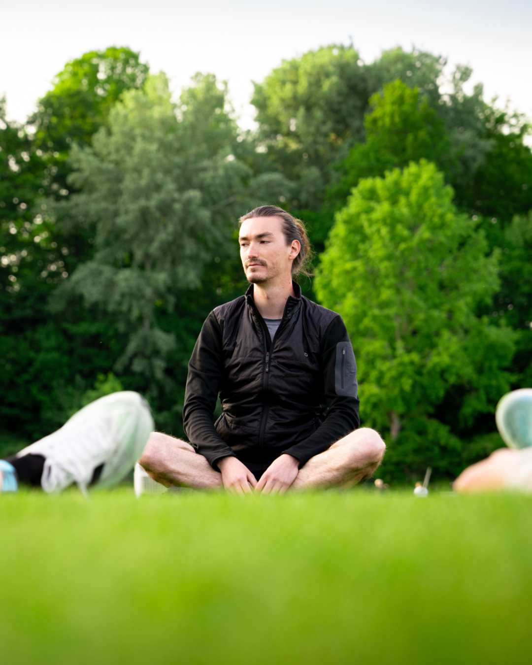 Tobias von WAAGWERKE sitzt im Schneidersitz auf der Wiese und leitet eine Entspannungsübung zum Sport-Mentaltraining am Ende des Lauftrainings an.